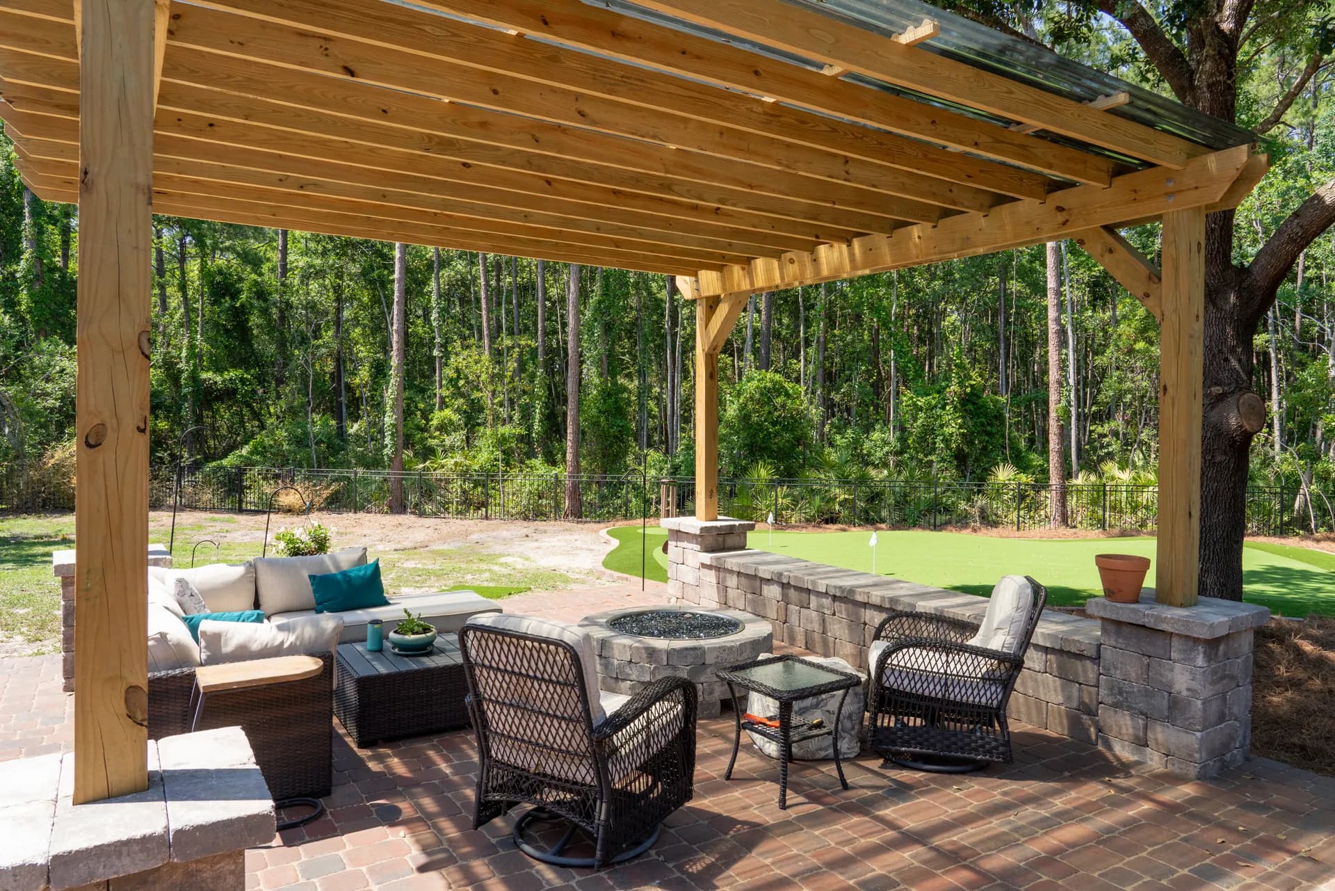 A wood pergola over fire-pit seating with a putting green beyond