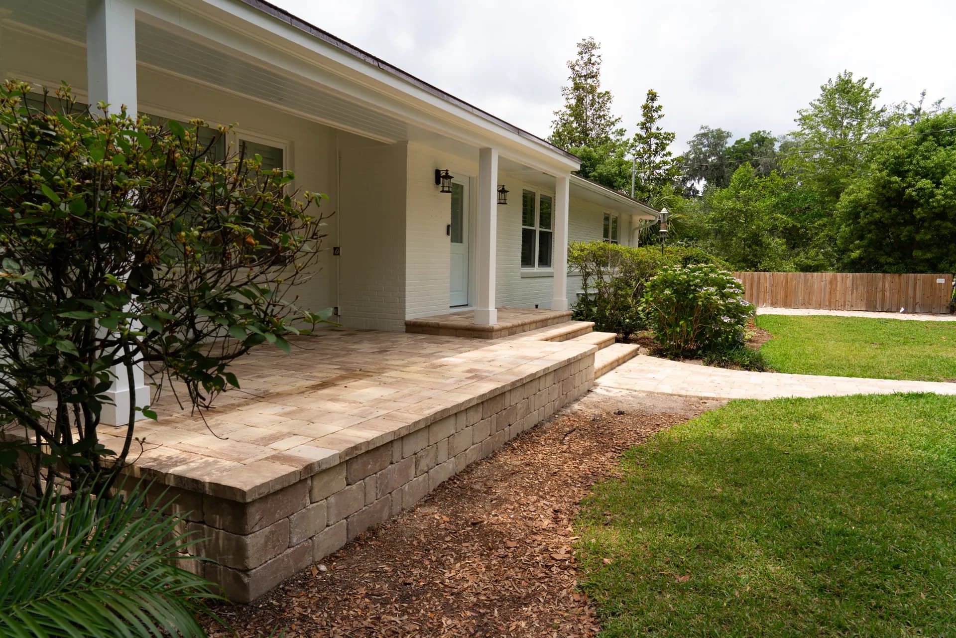 A new paver porch and stacked retaining wall at the front of a white house