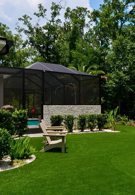A screen enclosure set on a stone knee wall beside a landscaped lawn