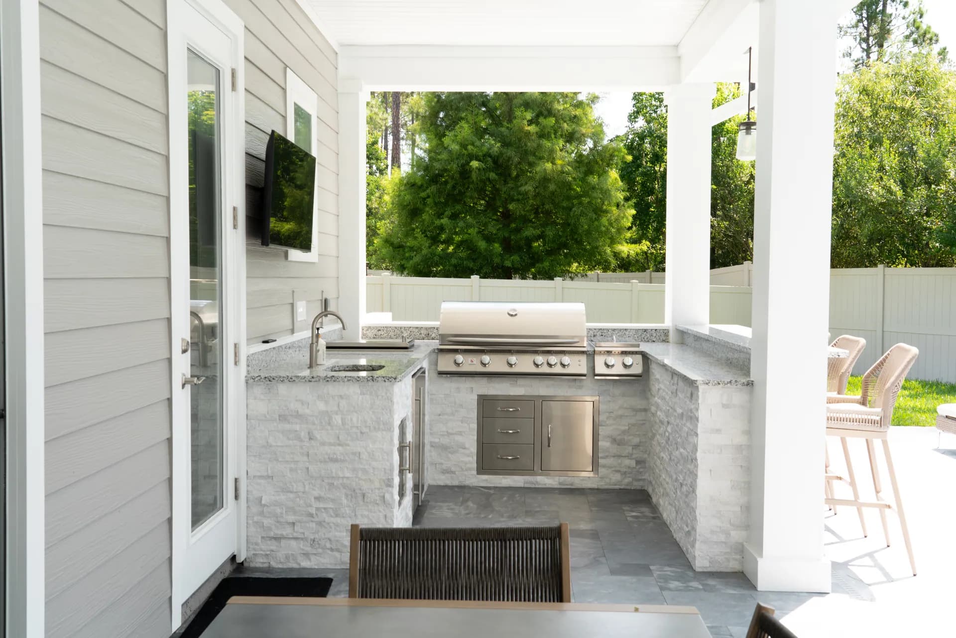 A covered patio outdoor kitchen faced in stacked stone with a grill and television