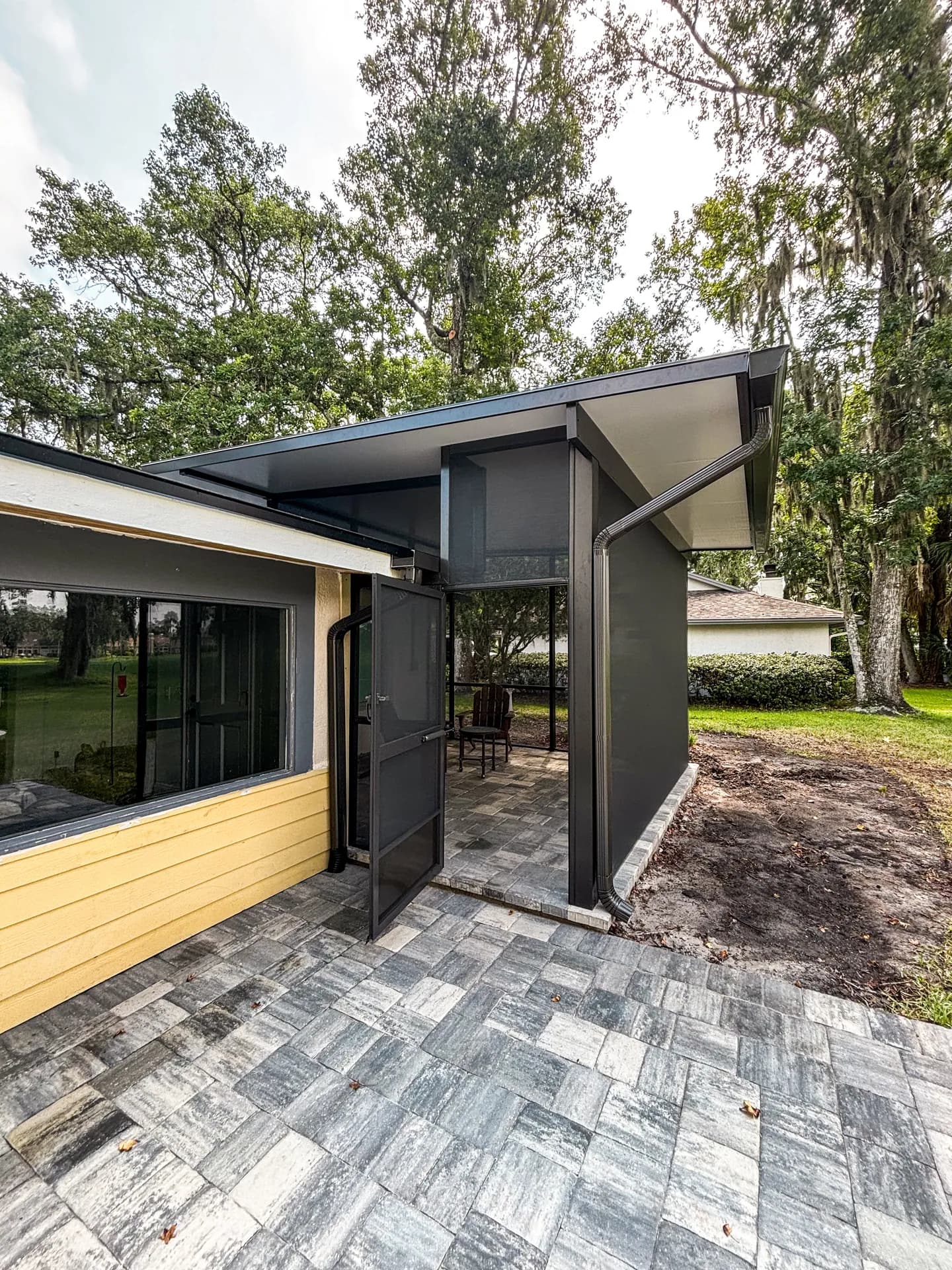 A gray paver patio wrapping a modern screened porch