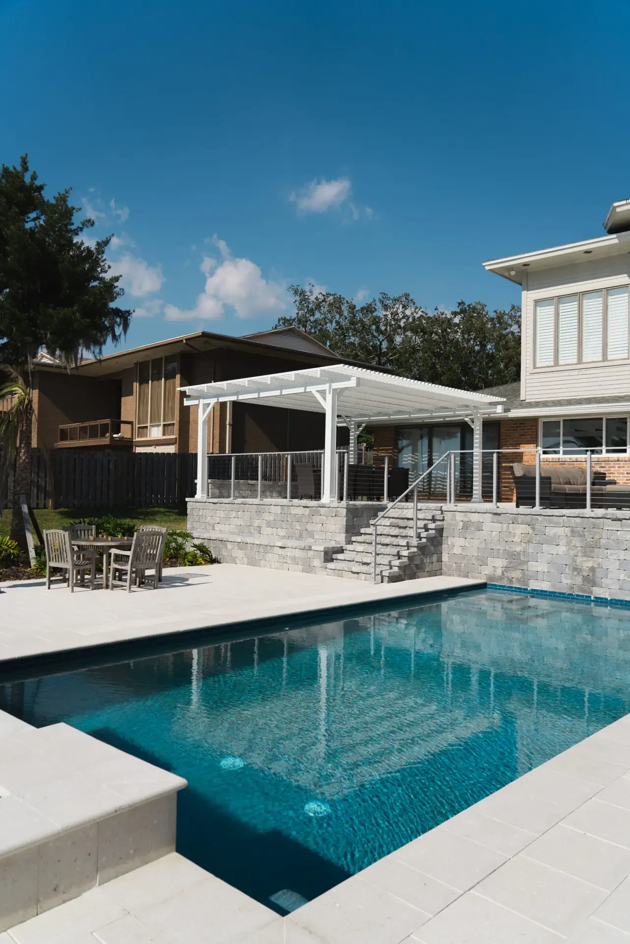 A white pergola over a raised patio with the pool below
