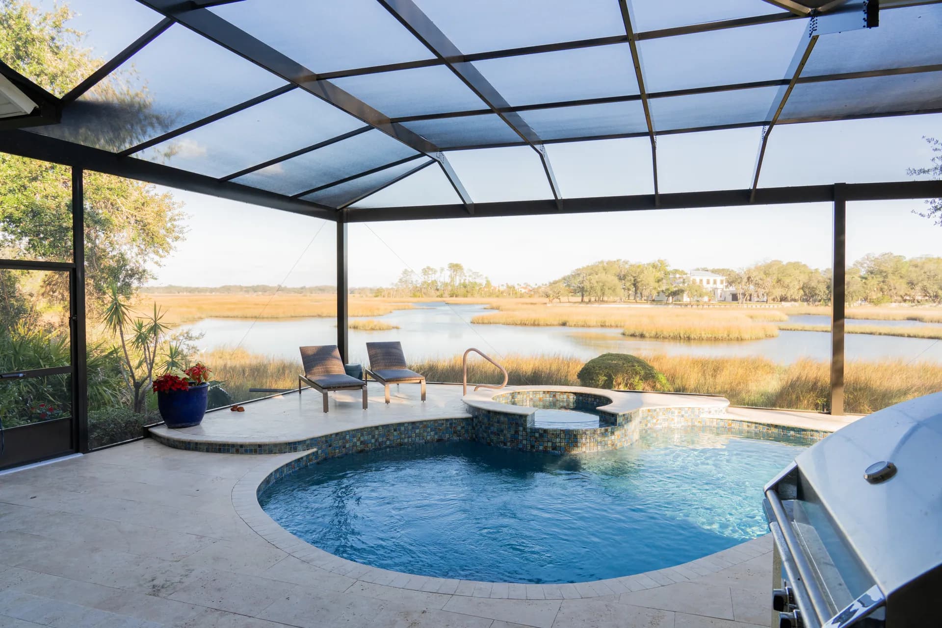 A travertine pool deck surrounding a pool and spa overlooking the marsh