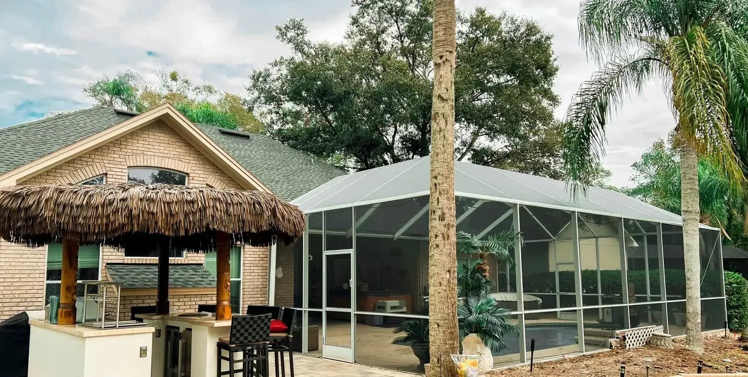 A screened pool enclosure beside a home and tiki bar