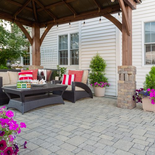 Brussel block design pavers on an exterior patio and summer living space with a covered gazebo, colorful petunias and comfortable seating